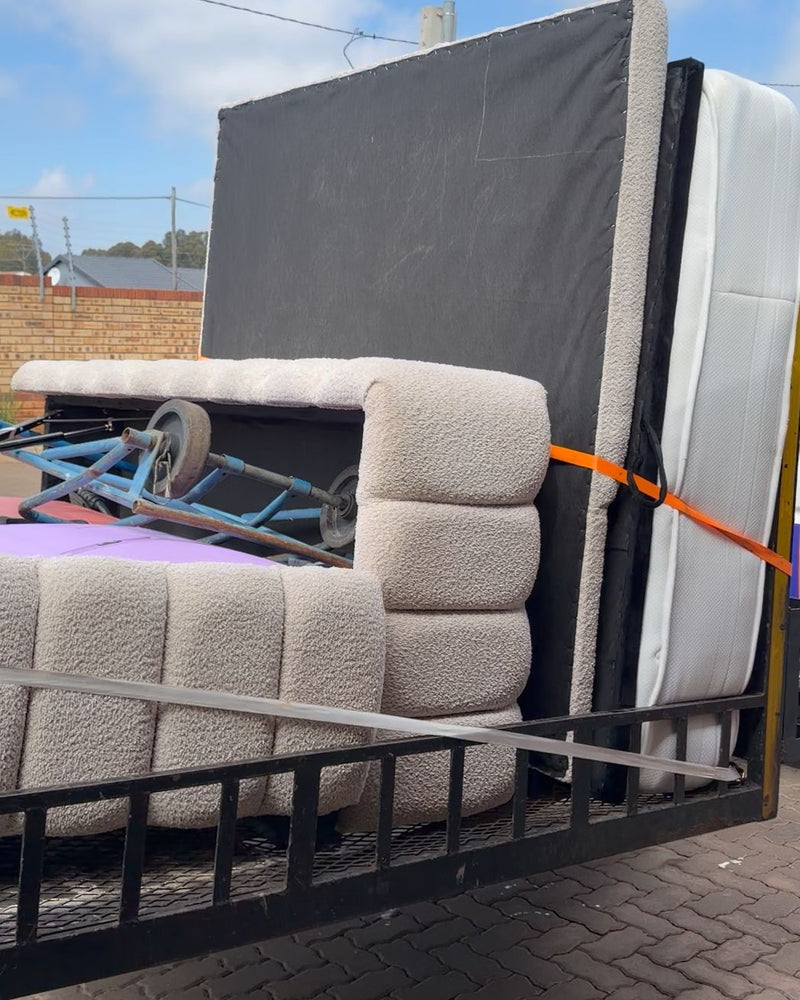 A couch, a mattress and an upholstered base strapped upright on the trailer for a furniture move
