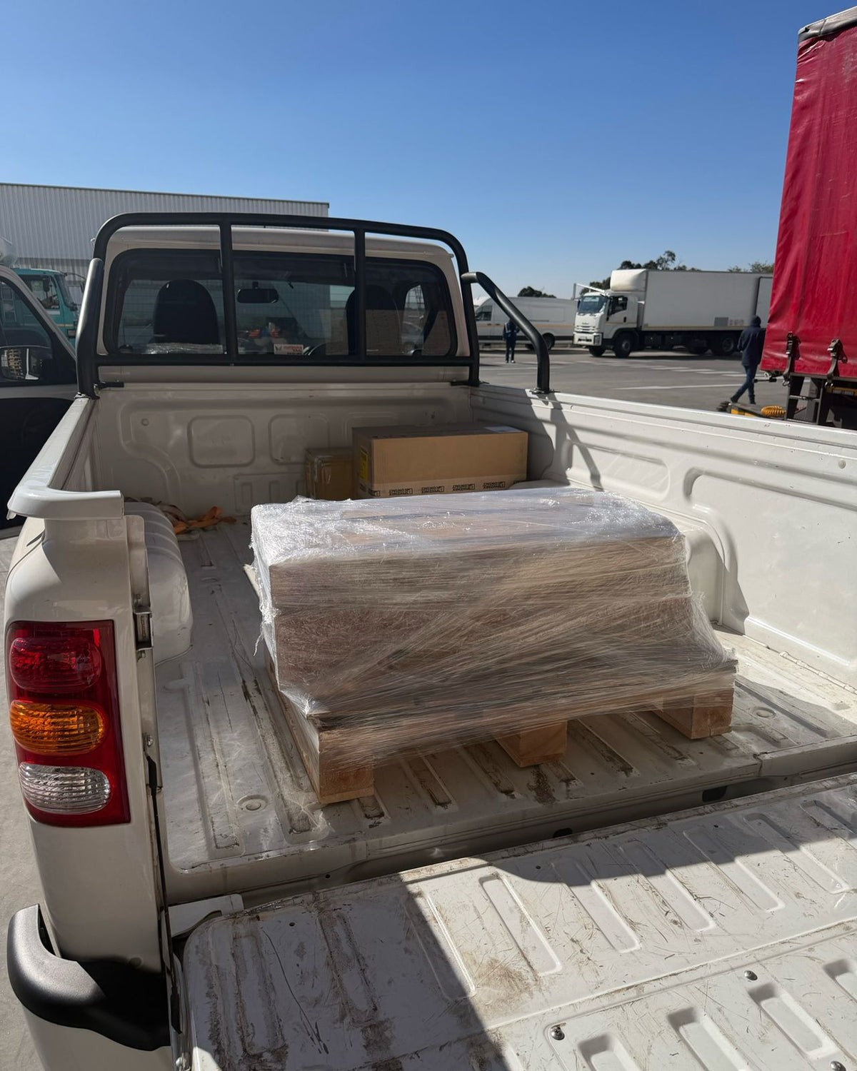 A shrink-wrapped pallet of boxed goods in the load bed of the bakkie at a truck yard
