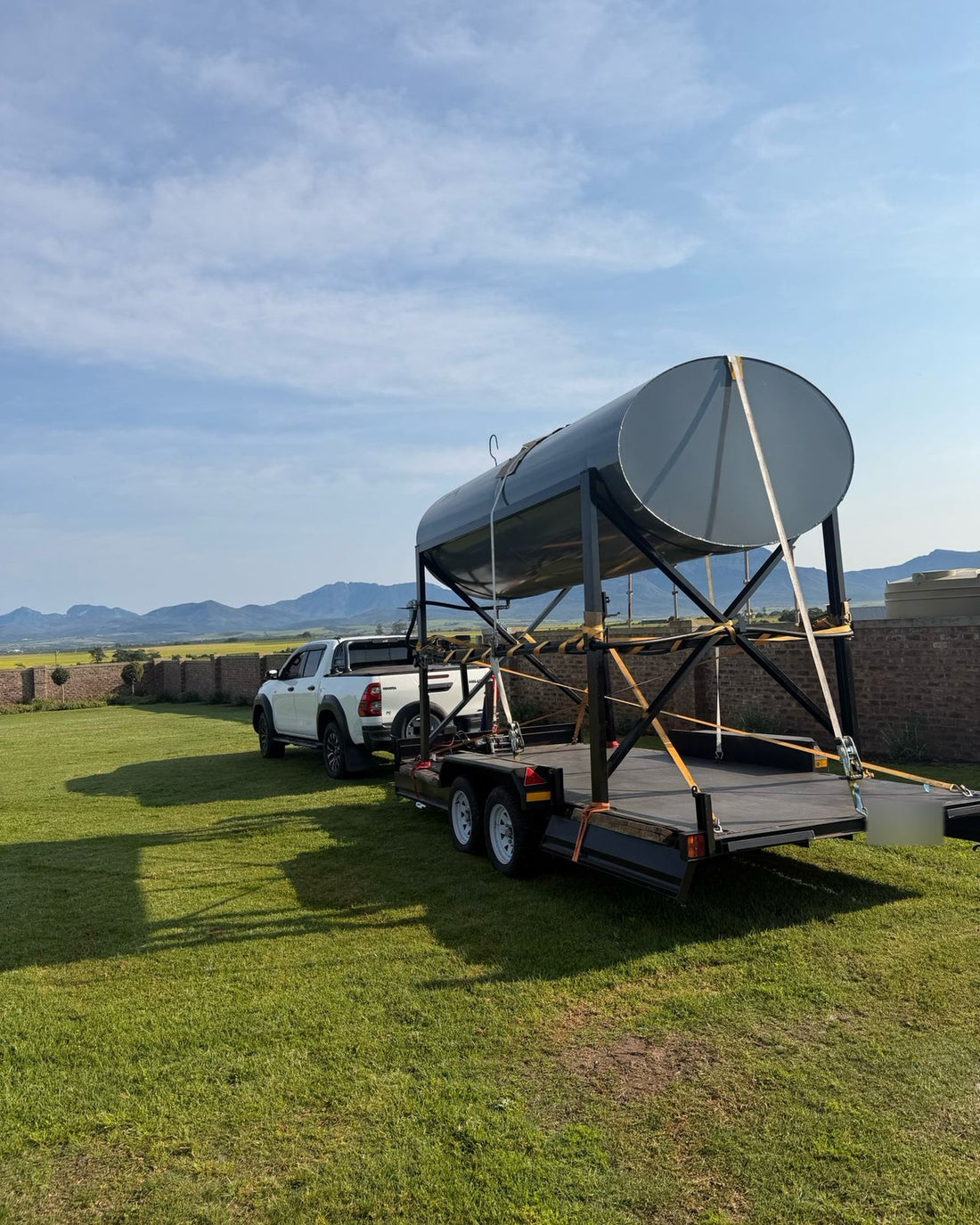 A large steel tank on a steel stand, strapped down on the double-axle trailer, with mountains behind