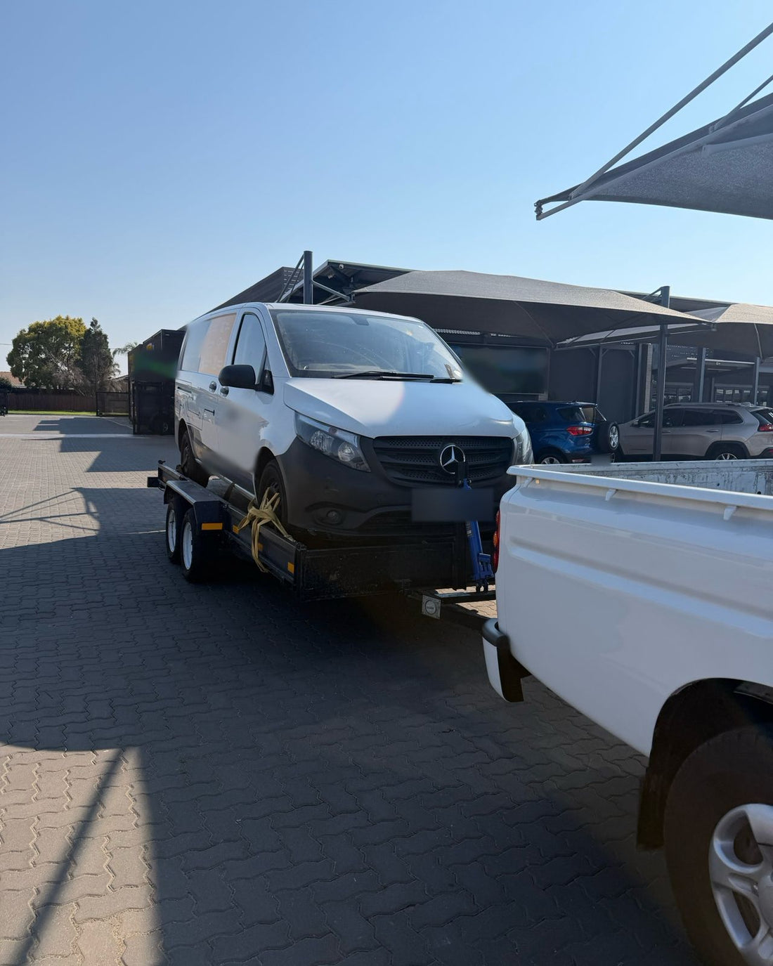 A customer's white Mercedes-Benz panel van strapped onto the car trailer behind the bakkie
