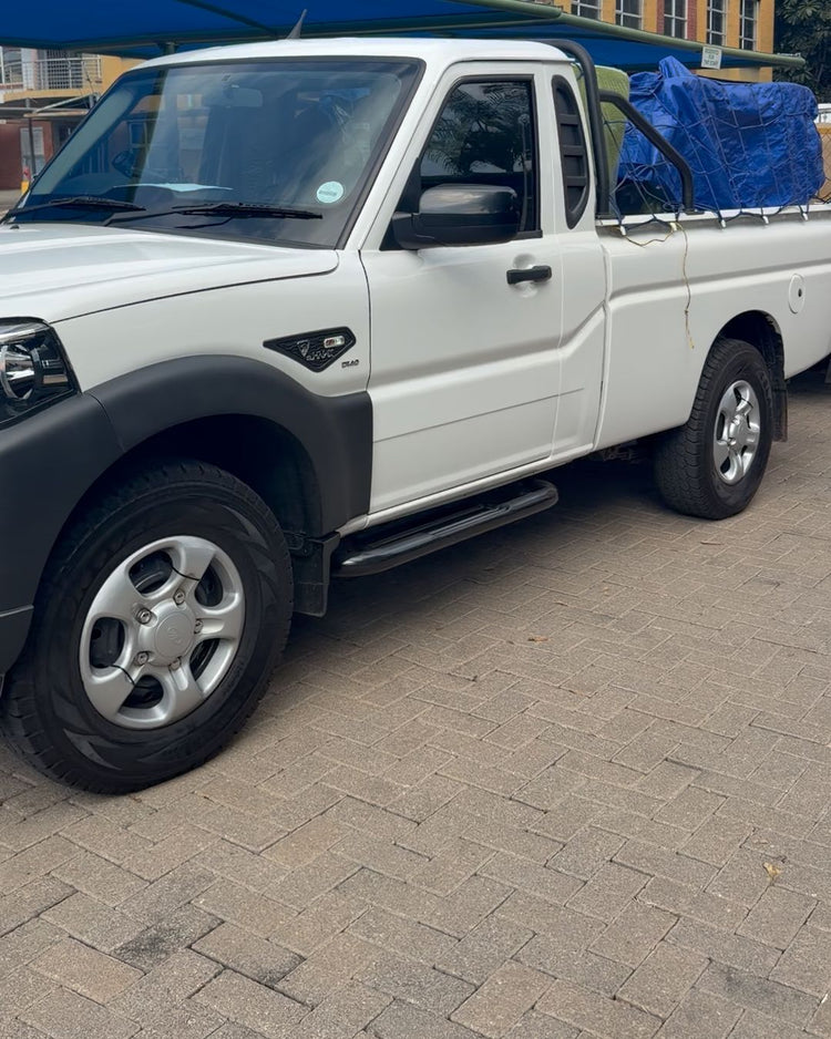 The white Mahindra S4 bakkie with a load under a blue tarpaulin, parked outside an office building
