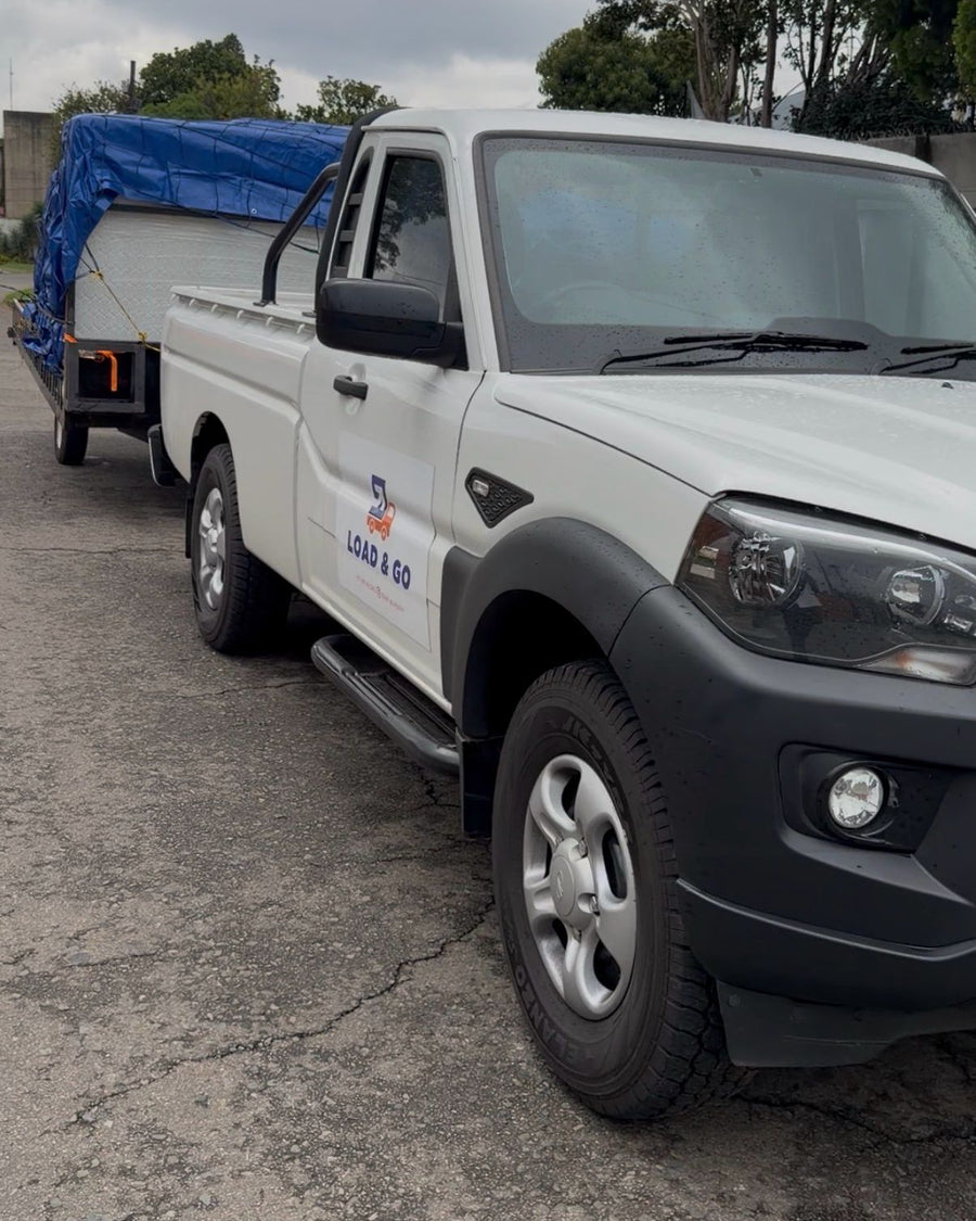 The branded Load & Go Mahindra S4 bakkie towing the double-axle trailer, its load covered with a blue tarpaulin