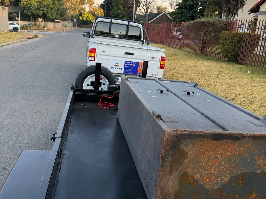 View along the double-axle trailer deck, with a steel bin strapped on, to the Load & Go Mahindra S4 bakkie towing it